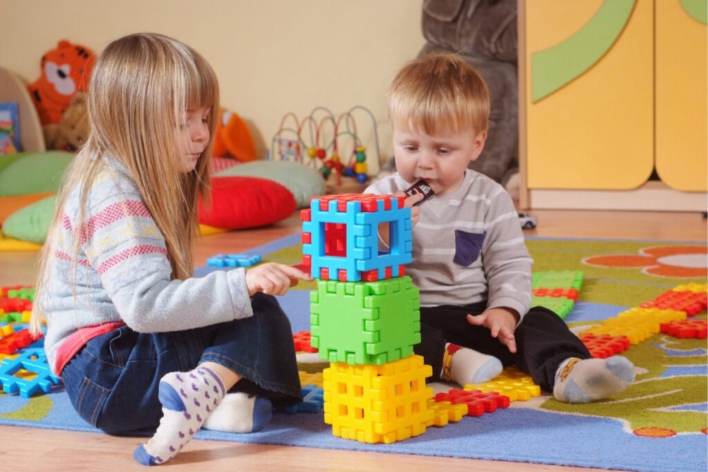 Young children building a tower with colourful construction blocks during indoor play at a nursery.