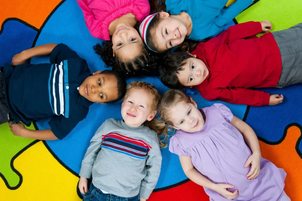 Group of children lying together on a colourful play mat during a nursery group activity.